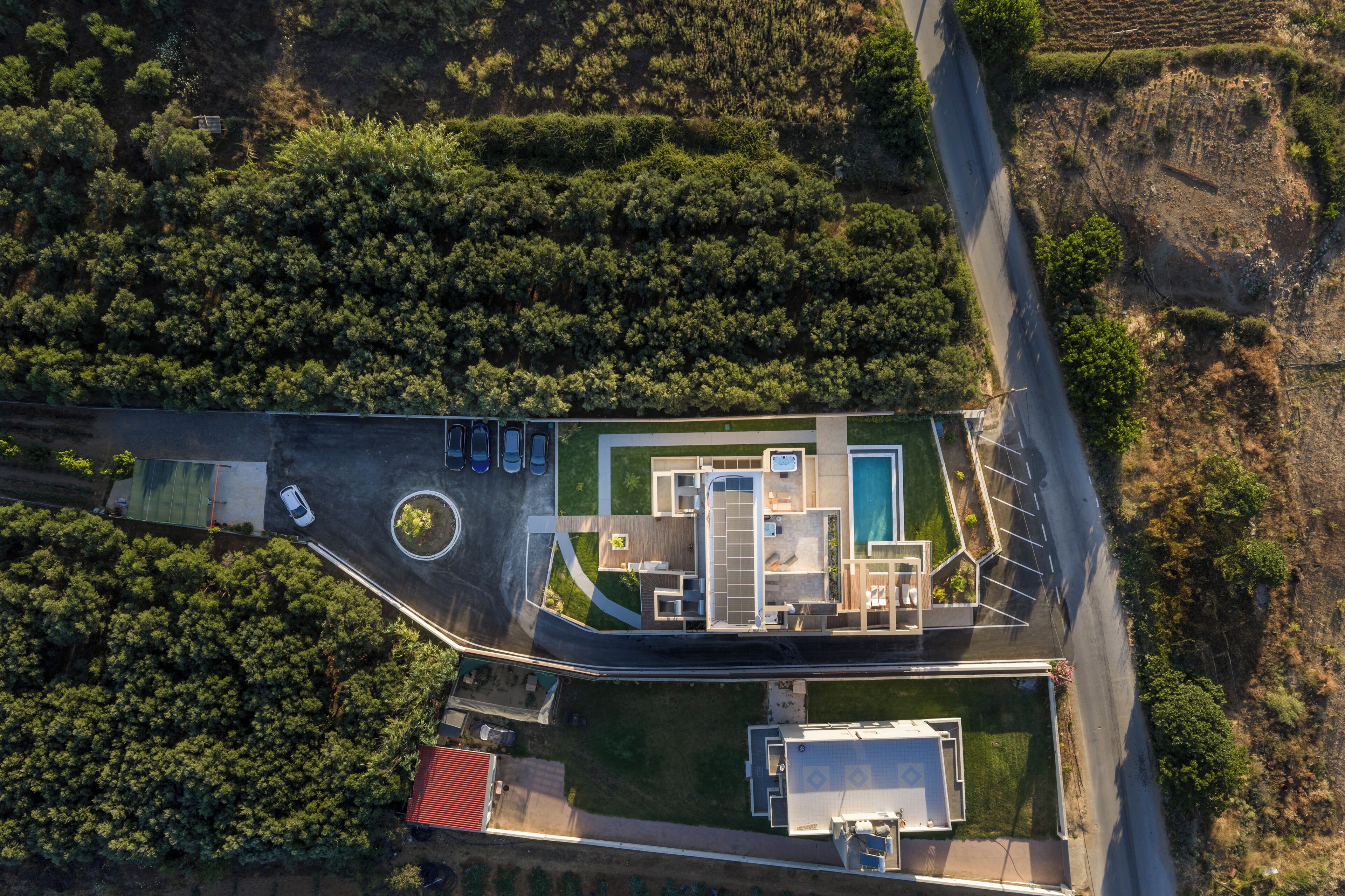 An aerial view of a property with a swimming pool, parking area, and a building with a flat roof.