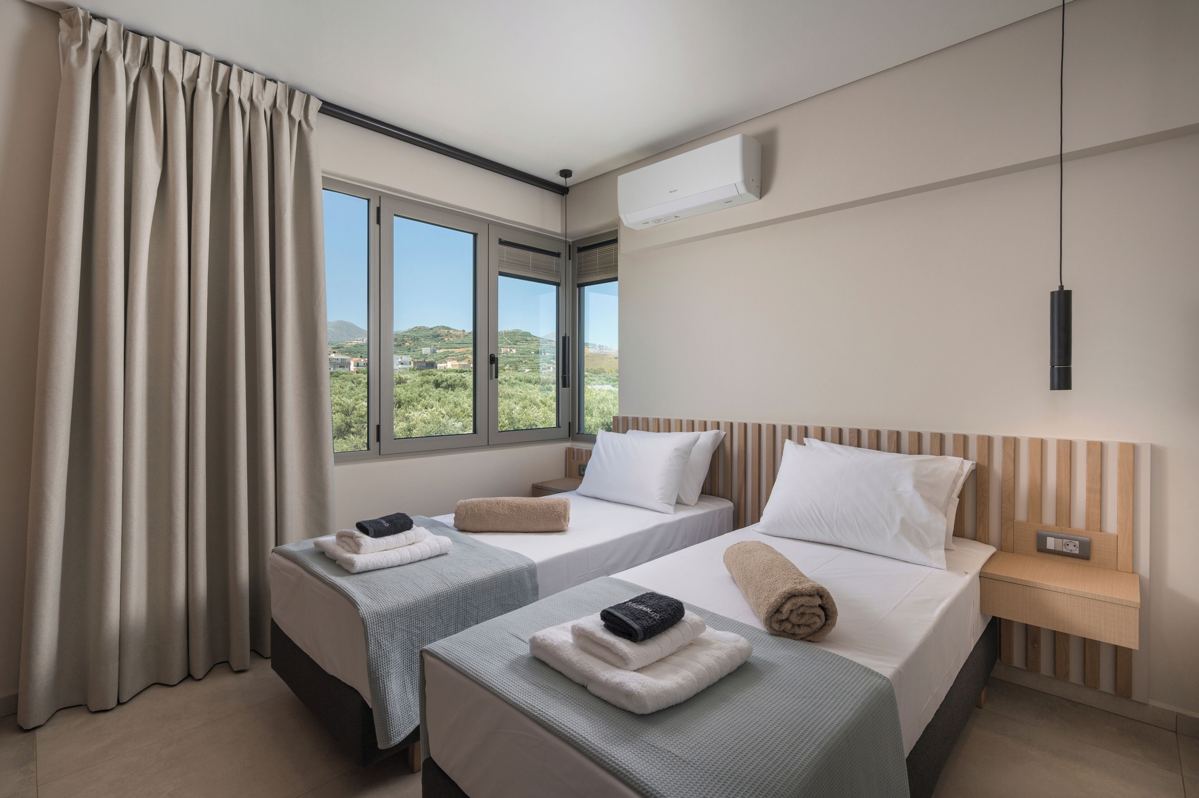 A hotel room with two beds, a window with a view, an air conditioning unit, and a bedside table.