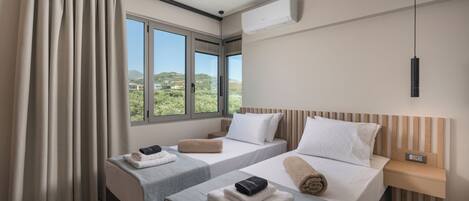 A hotel room with two beds, a window with a view, an air conditioning unit, and a bedside table.