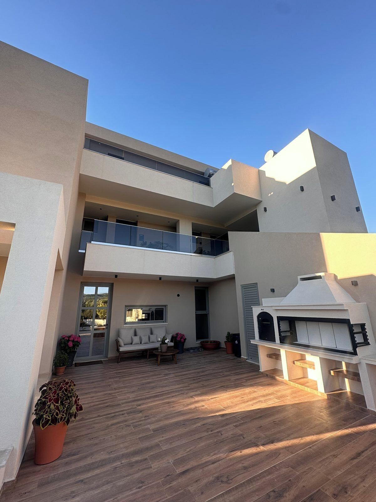 A modern two-story building with a flat roof, a balcony, and a barbecue area.