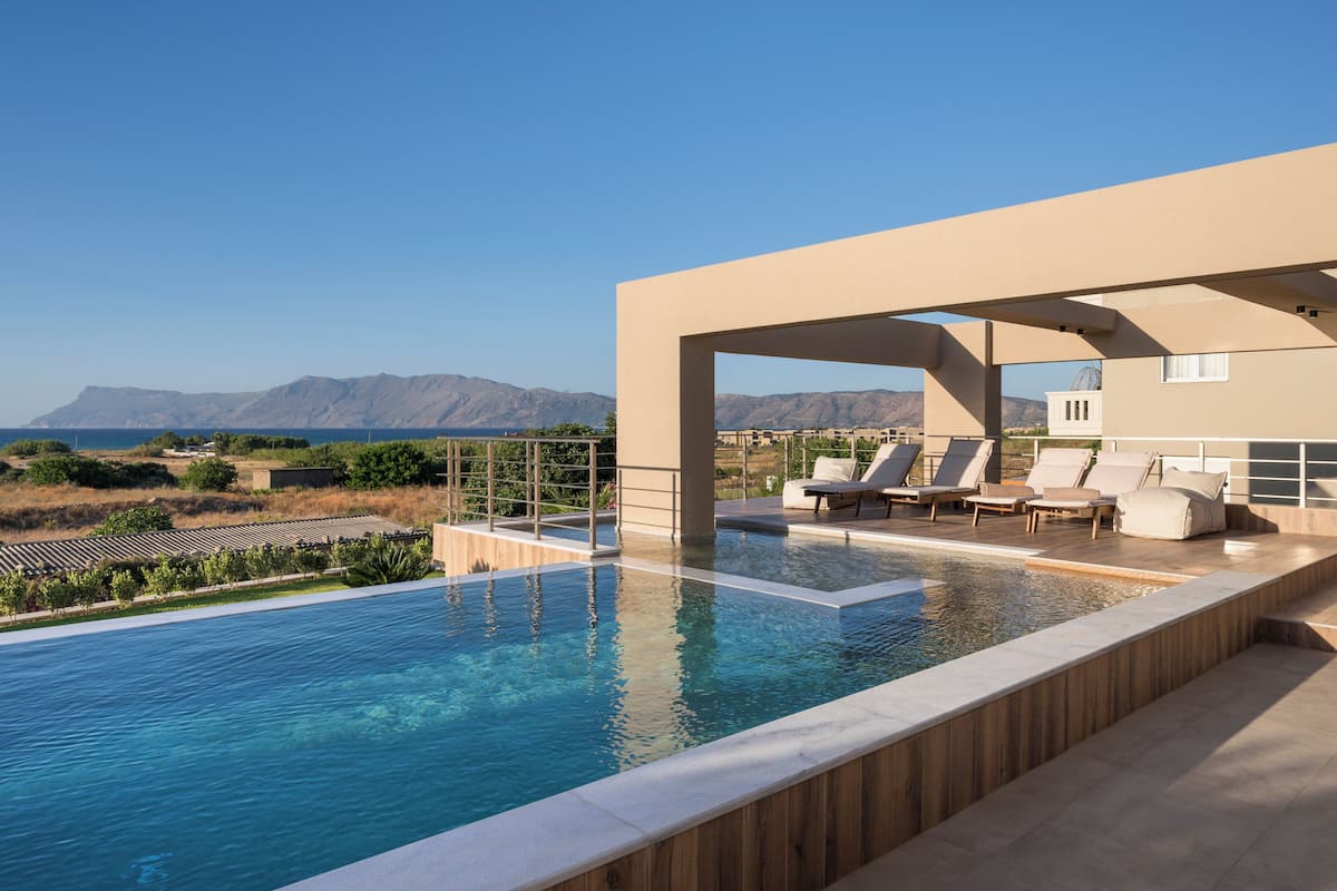 A swimming pool with lounge chairs, a view of mountains, and a clear sky.