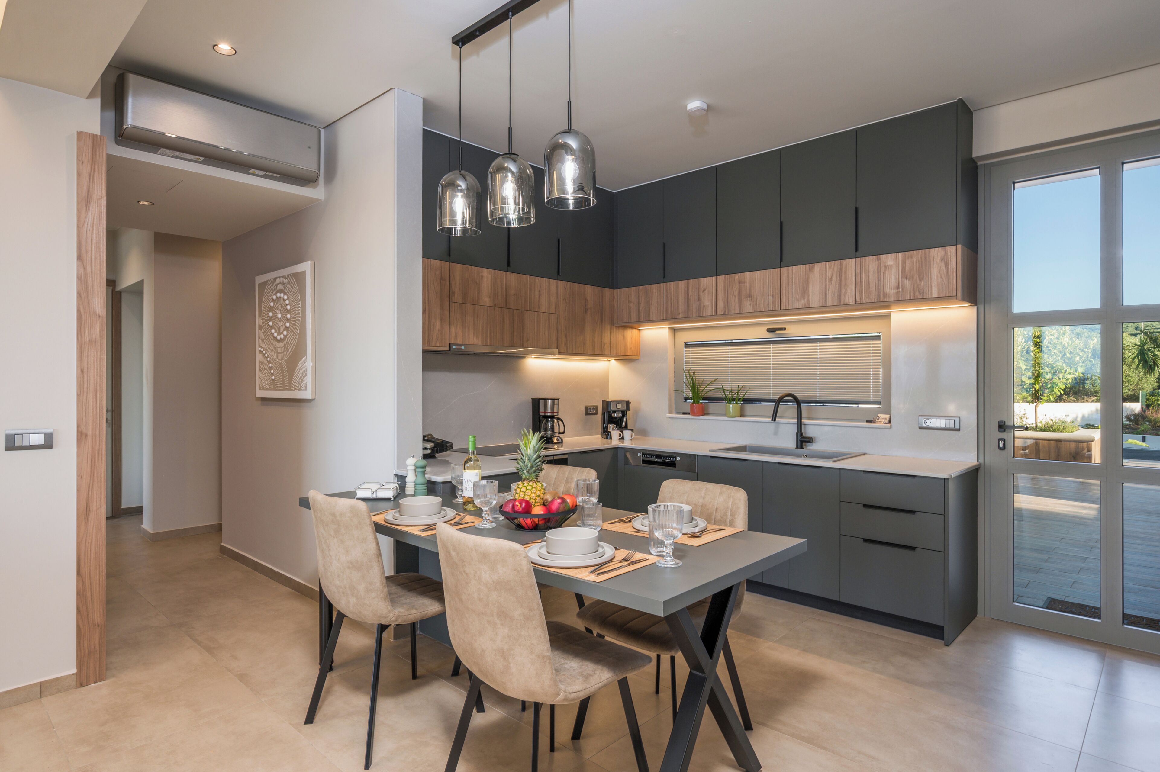 Une cuisine moderne avec des meubles de couleur sombre, une table à manger accompagnée de chaises et des luminaires suspendus.