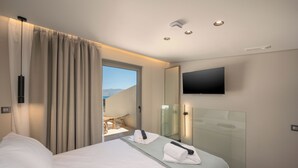 A hotel room with a bed, a TV, a glass shower enclosure, and a view of the outdoors. - The New Life Houses (Kissamos)
