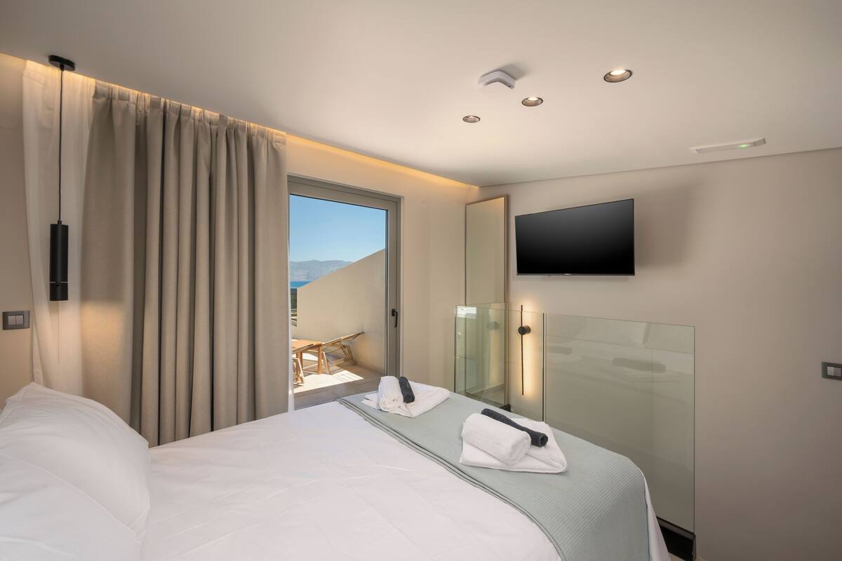 A hotel room with a bed, a TV, a glass shower enclosure, and a view of the outdoors.