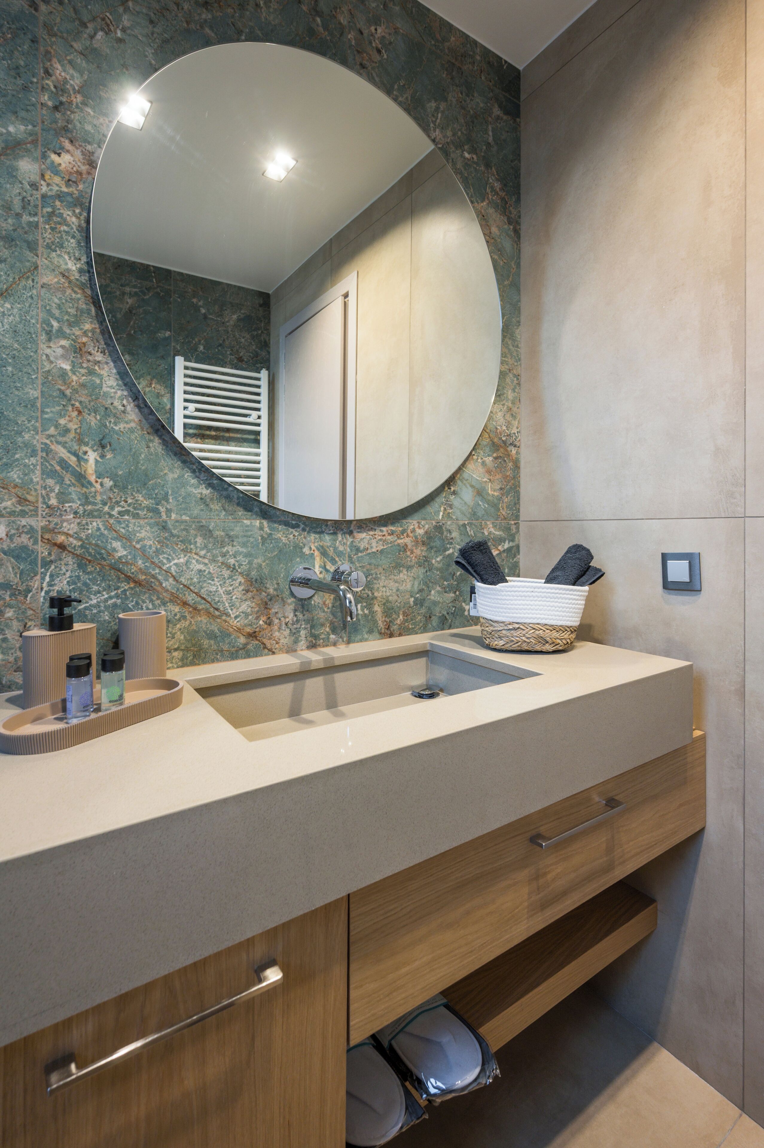 A bathroom with a marble backsplash, a round mirror, a double sink, and a towel rack.