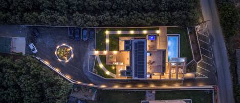 An aerial view of a modern building with a pool, solar panels, and a parking lot.