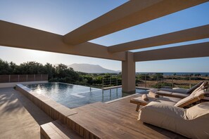 Una piscina d'infinity al terrat amb terrassa de fusta i gandules.