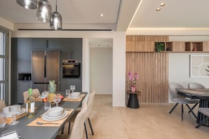 Una cocina moderna con refrigerador, horno y microondas integrados. Hay un comedor con una mesa preparada para cuatro, incluyendo platos, vasos y cubiertos.
