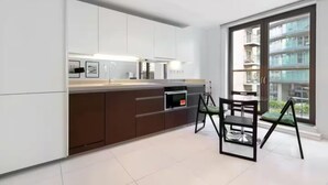Una cocina moderna con una isla marrón oscuro, armarios blancos y un ventanal con vistas a un edificio.