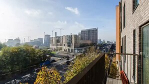 Un edificio moderno con jardín en la azotea, rodeado de otros rascacielos y una calle concurrida abajo.