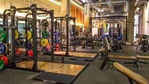 Un gimnasio con equipo de levantamiento de pesas, bancos y un espejo grande.