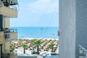 A beach view from a balcony with sun loungers and umbrellas, a clear sky, and the sea. - BF Home Plazh Apartment (Durrës)
