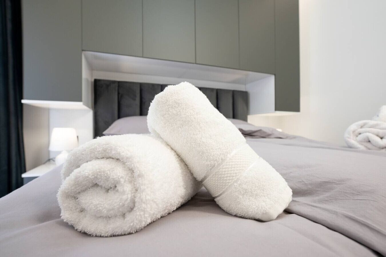 A neatly made bed with a grey bedspread and a white headboard.