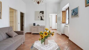 A living room with a sofa, a vase of sunflowers, a chandelier, and artwork on the walls. - Apartment Franca in Villa Pini with Shared Pool (Sarzana)
