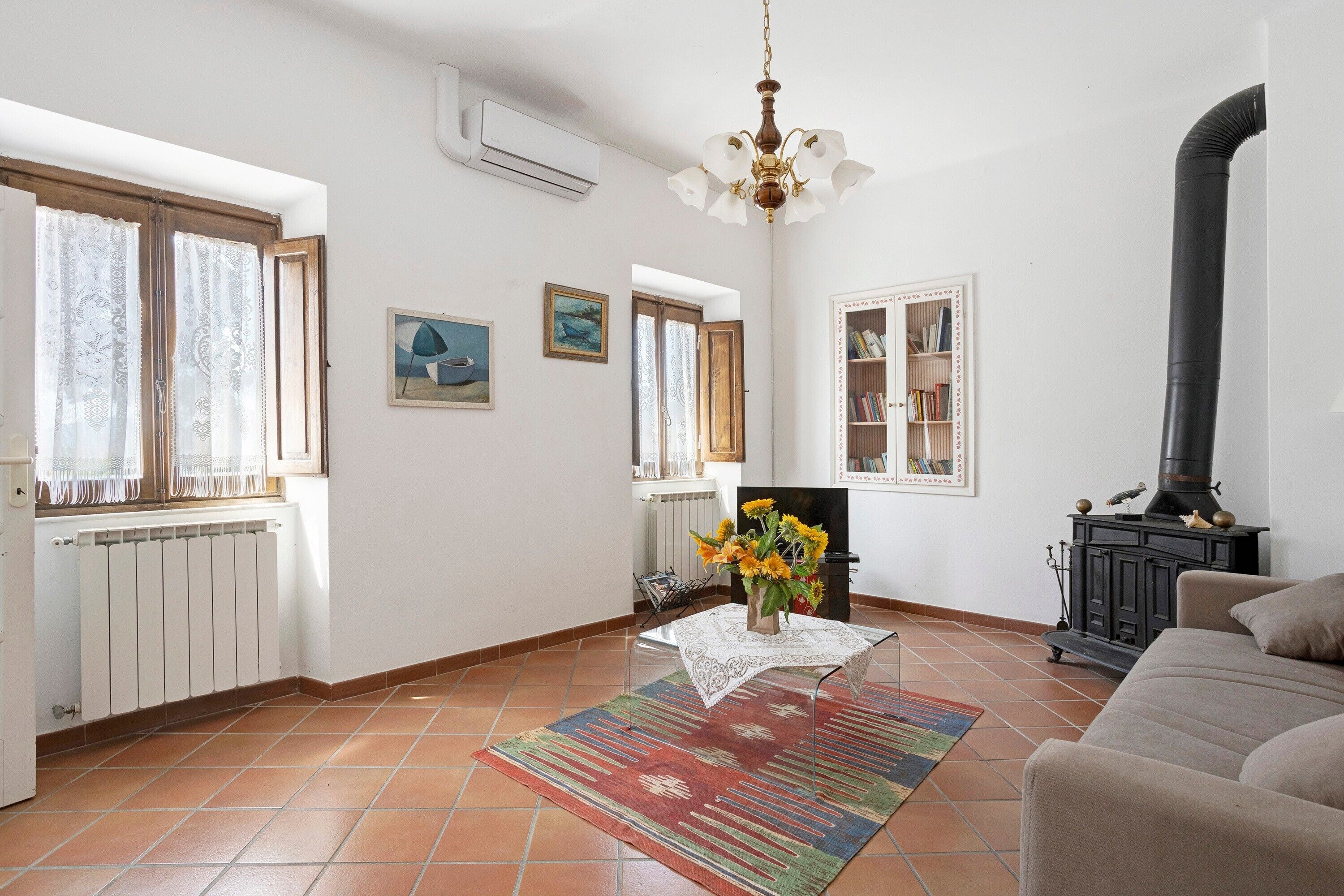Una sala de estar con chimenea, un radiador, un sofá, una mesa de centro con flores y una estantería.