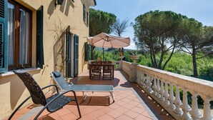 Eine Terrasse mit Tisch und Stühlen, einem weißen Geländer und Bäumen im Hintergrund.