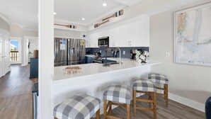 Uma cozinha moderna com armários brancos, uma ilha grande com banquetas, eletrodomésticos de aço inoxidável e um mapa na parede.