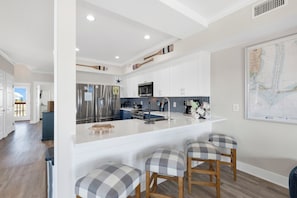 A modern kitchen with white cabinets, a large island with bar stools, stainless steel appliances, and a map on the wall. - Gulf Front Duplex | Pet Friendly | Private Hot Tub (Fort Morgan)