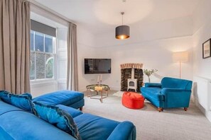 A modern living room with a blue sofa set, a red bean bag, a small table with a lamp, and a television on the wall. - Skylark Apartment Bowness (Bowness-on-Windermere)