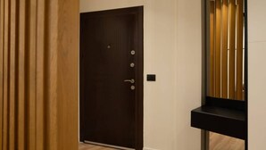 Una puerta de madera oscura con manija y cerradura, un interruptor de luz y un panel de madera a la izquierda.