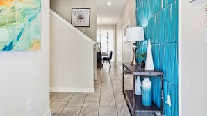 A hallway with a teal accent wall, a framed artwork, and a console table with decorative items. - Spacious 4-Bedroom Townhome with PS5, Private Pool & BBQ Grill at Storey Lake (Kissimmee)