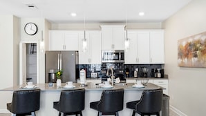 A modern kitchen with white cabinets, stainless steel appliances, and a central island with bar stools. - Spacious 4-Bedroom Townhome with PS5, Private Pool & BBQ Grill at Storey Lake (Kissimmee)