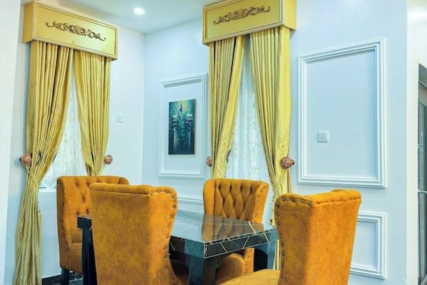 A dining area with a table and four chairs, featuring a decorative ceiling and curtains.