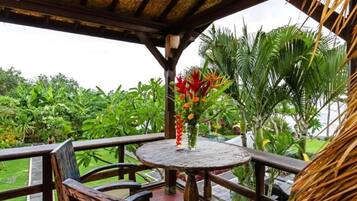 A wooden deck with a round table and chairs, surrounded by lush tropical vegetation.