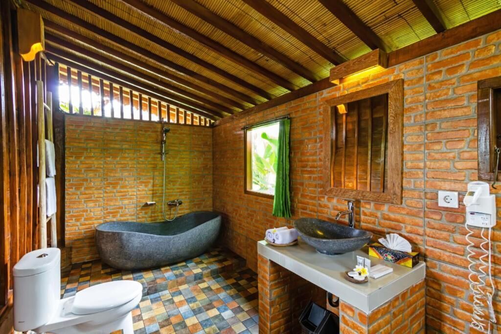 Un bagno con una vasca da bagno in pietra, un lavandino bianco e un pavimento piastrellato.