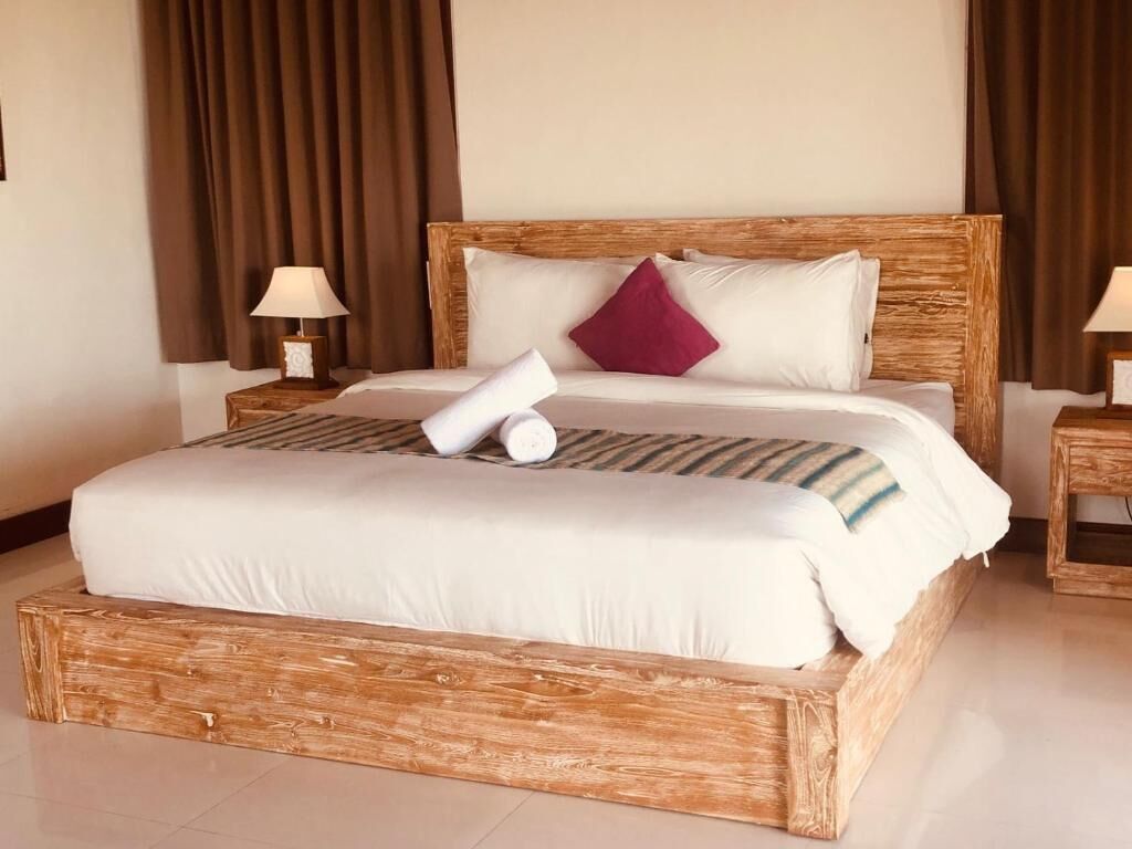 A large bed with a wooden frame, white bedding, and a single decorative pillow.