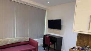 A compact living space with a sofa, a desk, a television, and a basket of snacks. - Heathrow Airport - Apt - Stay 3 - Great Location (Hounslow)