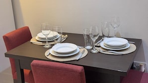 Taula de dinar coberta amb plats blancs, gots i coberts, envoltada de cadires tapissades de color vermell.