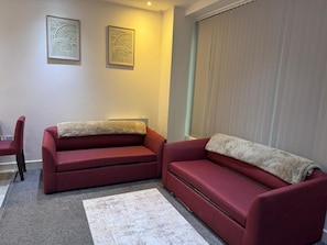 A room with two red sofas, a white rug, and two framed abstract art pieces on the wall. - Heathrow Airport - Apt - Stay 3 - Great Location (Hounslow)