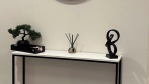 A minimalist console table with a round mirror above it, a bonsai tree, a small vase, and a decorative sculpture. - Heathrow Airport - Apt - Stay 3 - Great Location (Hounslow)