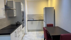A compact kitchen with white cabinets, a black countertop, and a red chair at a table. - Heathrow Airport - Apt - Stay 3 - Great Location (Hounslow)