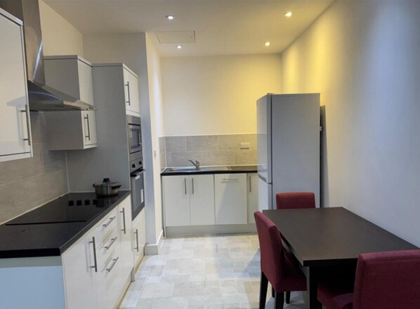 A compact kitchen with white cabinets, a black countertop, and a red chair at a table. - Heathrow Airport - Apt - Stay 3 - Great Location (Hounslow)