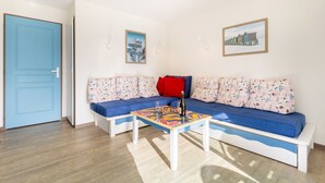 A room with a blue door, a sofa with patterned cushions, a table with a bottle, and two framed pictures on the wall. - La Parenthèse Bleue – Sea View and Pool (Fouesnant)
