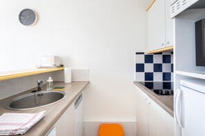 Une cuisine compacte équipée d’un évier, d’un grille-pain, d’un four à micro-ondes et d’un petit tabouret orange.