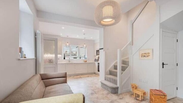 Een moderne woonkamer met een bank, een trap en een keuken op de achtergrond.