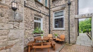 Een stenen gebouw met een houten patio tafel en stoelen, omgeven door stenen muren en ramen.