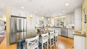 A modern kitchen with stainless steel appliances, a central island with bar stools, pendant lighting, and a view of the outdoors through a window. - Perfect For Families,Walk 2 Beach and Restaurants! (San Diego)