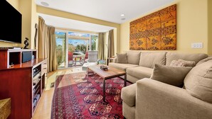 A living room with a sofa, coffee table, and TV. There is a large window with curtains, a patterned rug, and a wall art piece. - Perfect For Families,Walk 2 Beach and Restaurants! (San Diego)