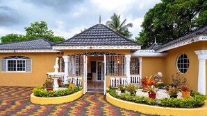 A two-story building with a tiled roof, a central entrance with a decorative gate, and a courtyard with a patterned walkway and potted plants. - Paradise Oasis - Ocho Rios (Tower Isle)