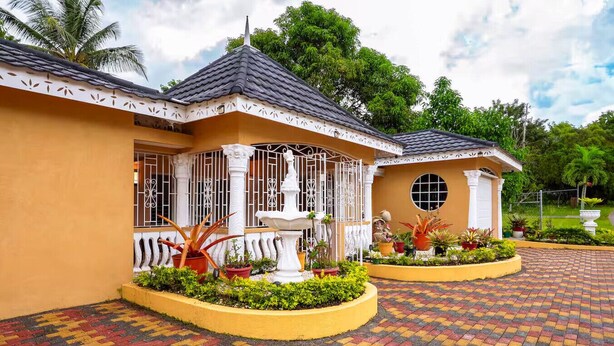 A two-story building with a tiled roof, a fountain, and a garden with various plants. - Paradise Oasis - Ocho Rios (Tower Isle)