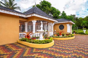 A two-story building with a tiled roof, a fountain, and a garden with various plants. - Paradise Oasis - Ocho Rios (Tower Isle)
