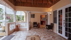 A covered patio with a tiled floor, white columns, and a view of the garden through the glass doors. - Paradise Oasis - Ocho Rios (Tower Isle)