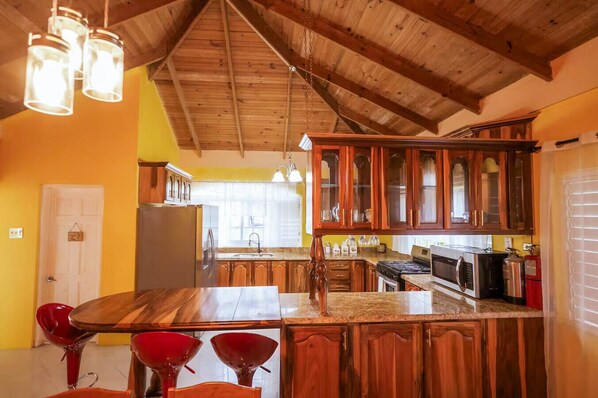 A kitchen with wooden cabinets, a central island, and a dining area with red chairs. - Paradise Oasis - Ocho Rios (Tower Isle)