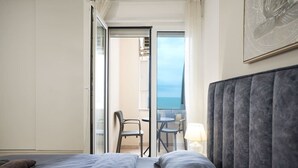A hotel room with a bed, a chair, and a table by a balcony with a view.
