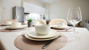 A dining table set with white plates, bowls, and cutlery, with a wine glass and a potted plant on the table.