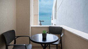 A balcony with a round table and two chairs, a potted plant, and a view of the sea and a pier.